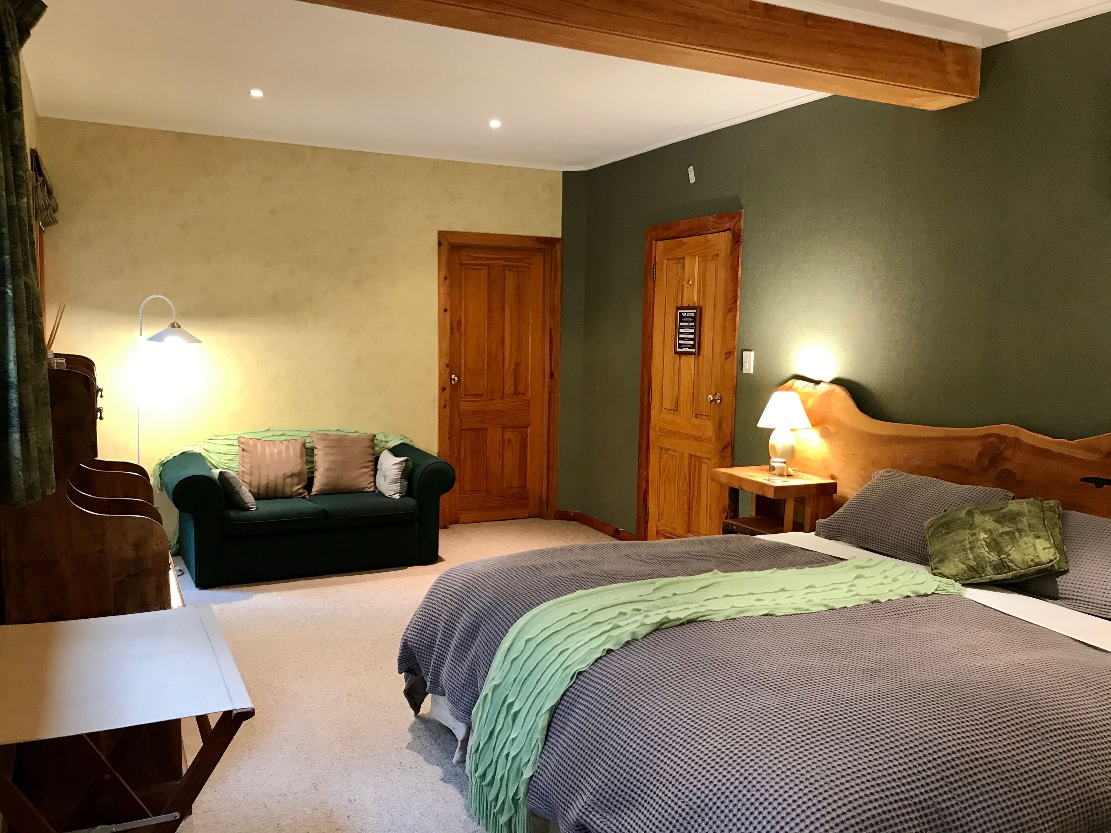 Une chambre à coucher avec un lit, un canapé vert, une porte en bois et une lampe.