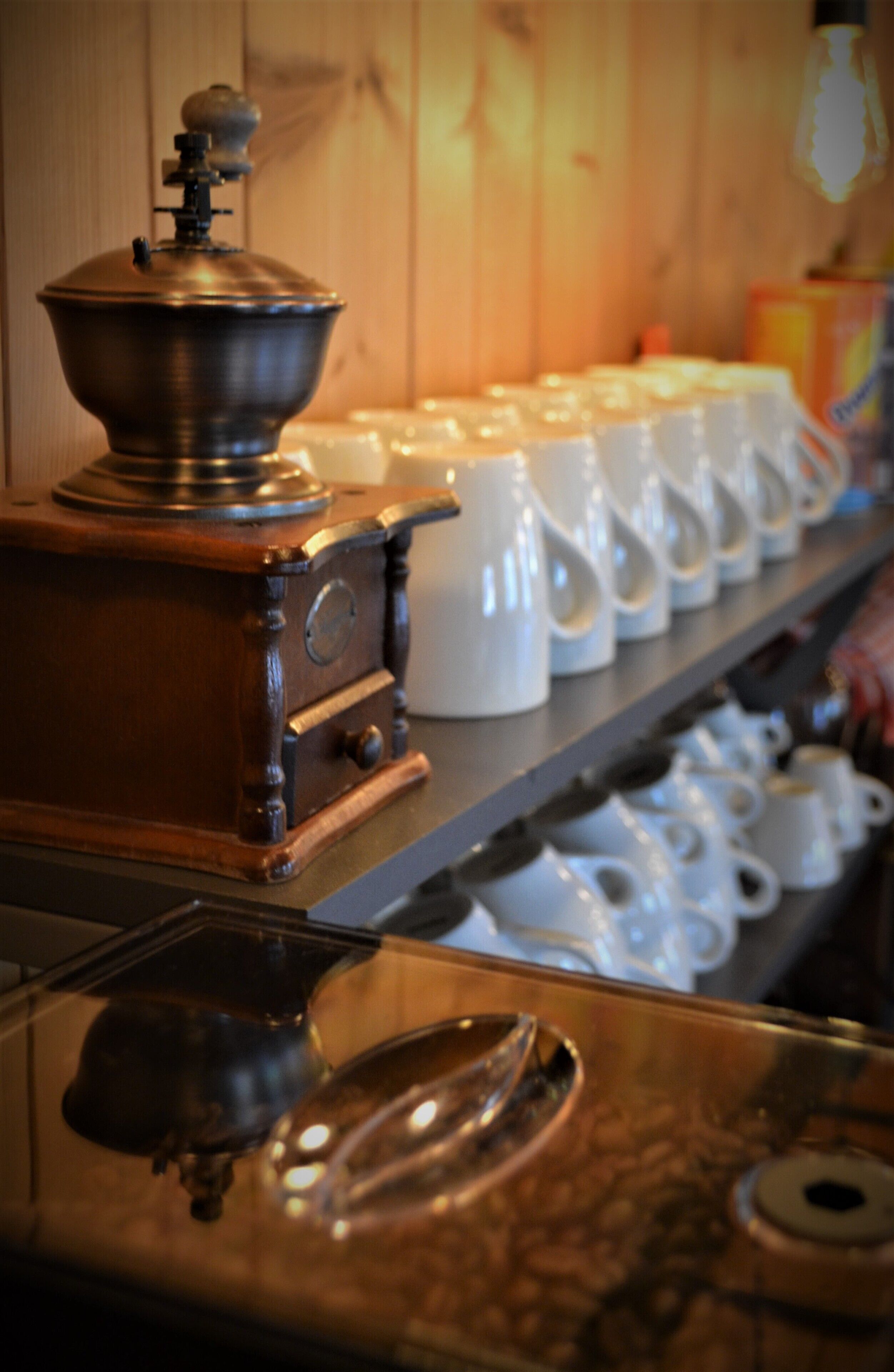 Una estación de café con una cafetera, una hilera de tazas blancas y un estante con tazas adicionales.
