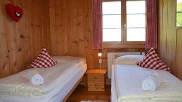 A wooden cabin room with two beds, each with a red and white checkered pillow, a heart-shaped decoration, and a lamp between the beds.