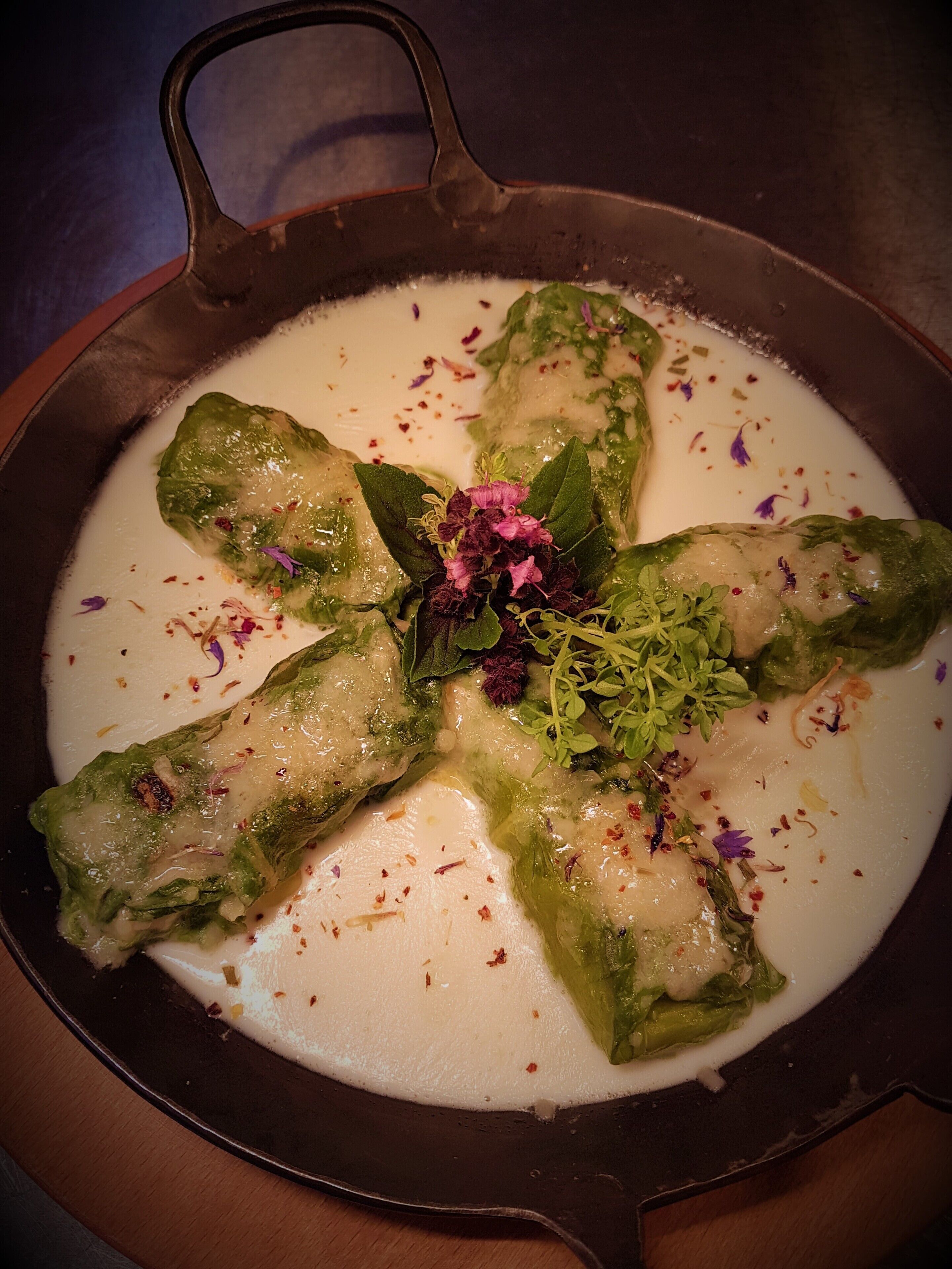 A dish of stuffed vegetables in a creamy sauce, garnished with herbs and flowers.