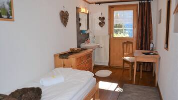 A bedroom with a bed, a wooden dresser, a desk, and a window with curtains.