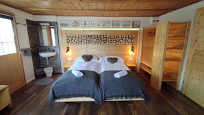 A double room with two beds, a wooden ceiling, a wooden wall with a log pattern, a sink, and a window. - Gasthaus Alpina (Tschappina)