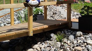 A wooden deck with a lifebuoy, rocky ground, and a rope barrier. - Gasthaus Alpina (Tschappina)