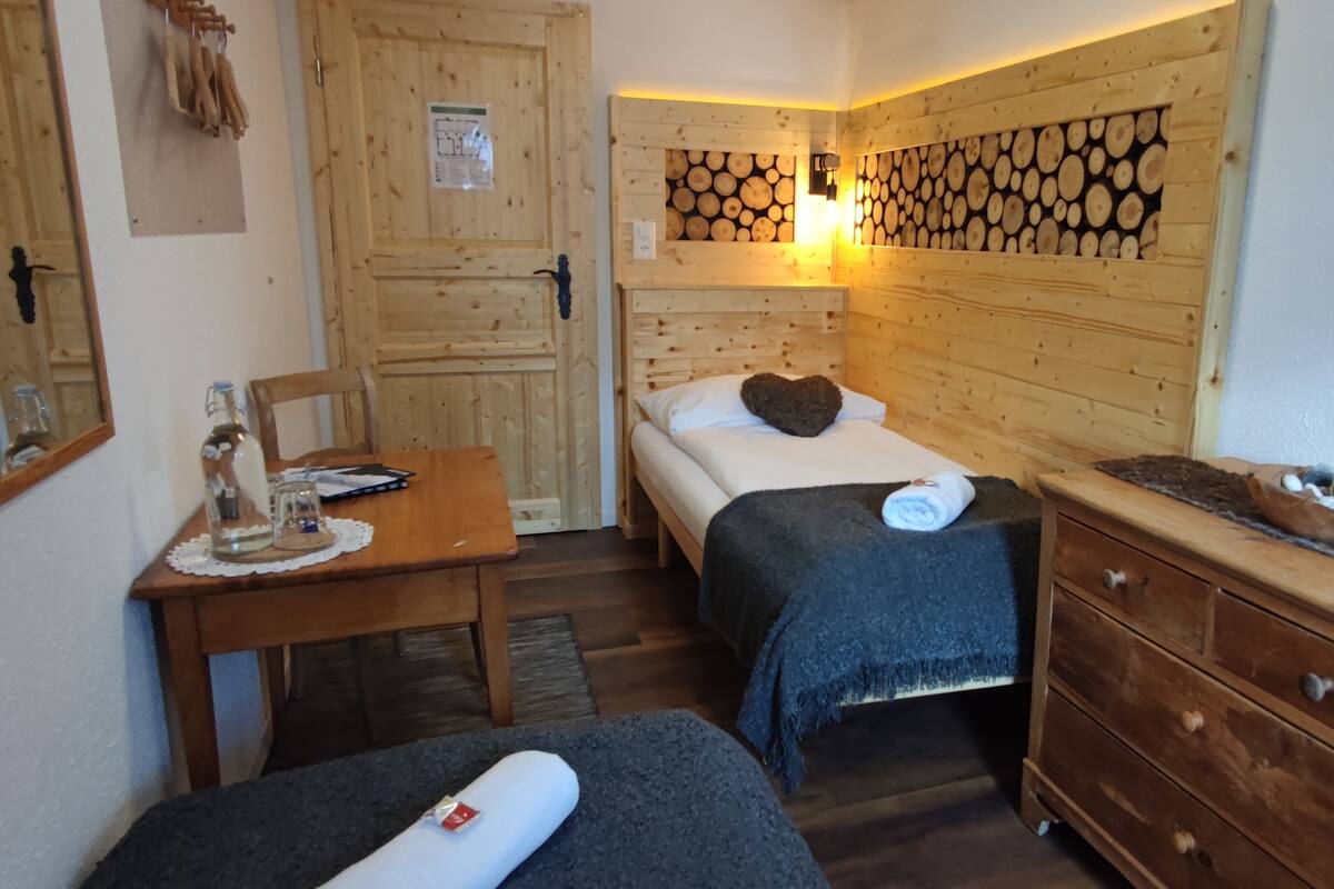 A wooden room with two beds, a wooden dresser, and a table with a bottle and glasses.