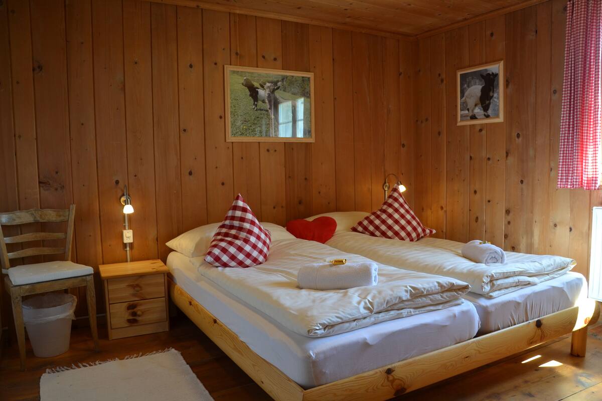 A wooden cabin bedroom with two beds, a nightstand, a chair, and a wooden floor.