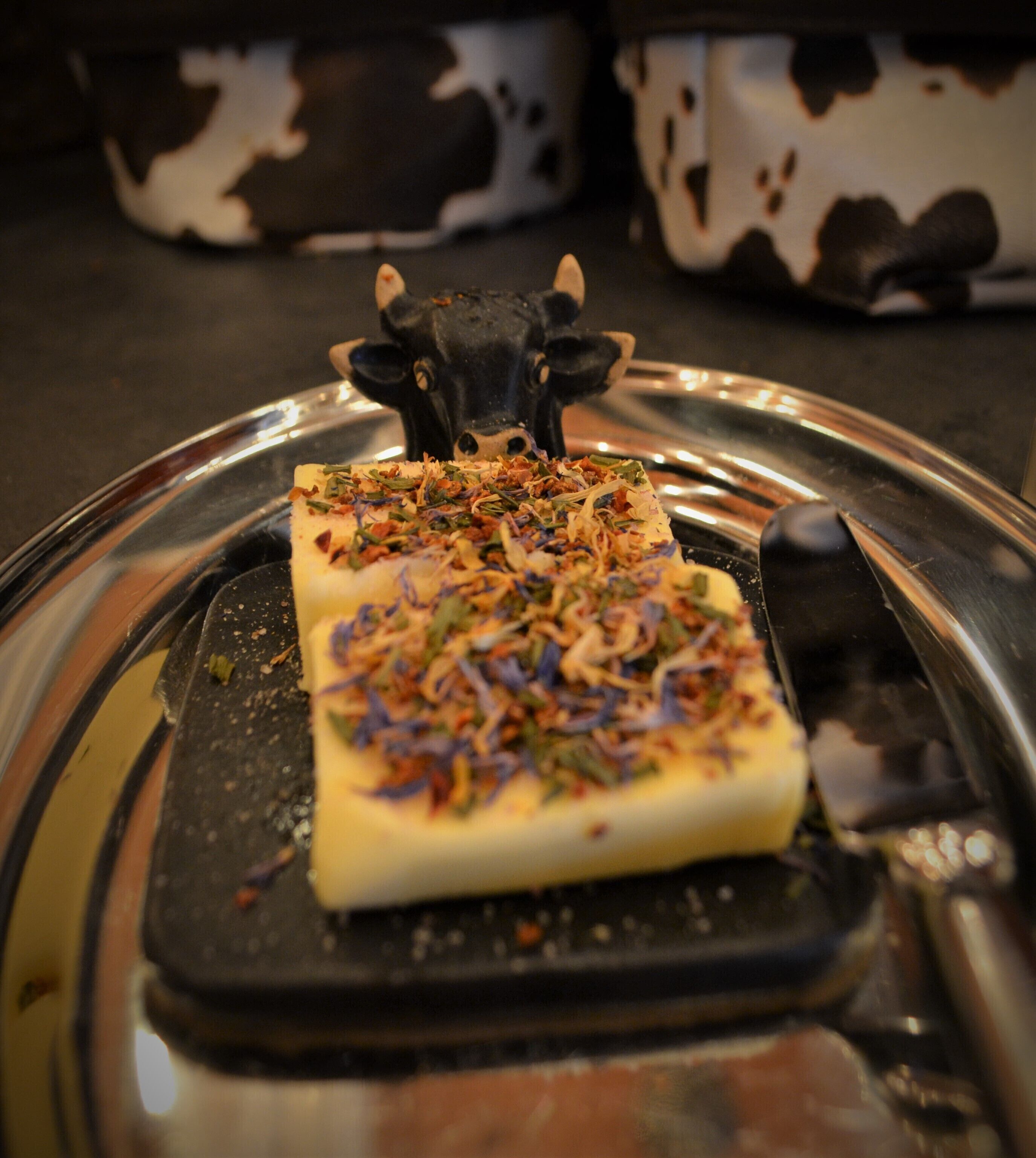 A rectangular block of food on a black cutting board with a cow-shaped decoration on top.