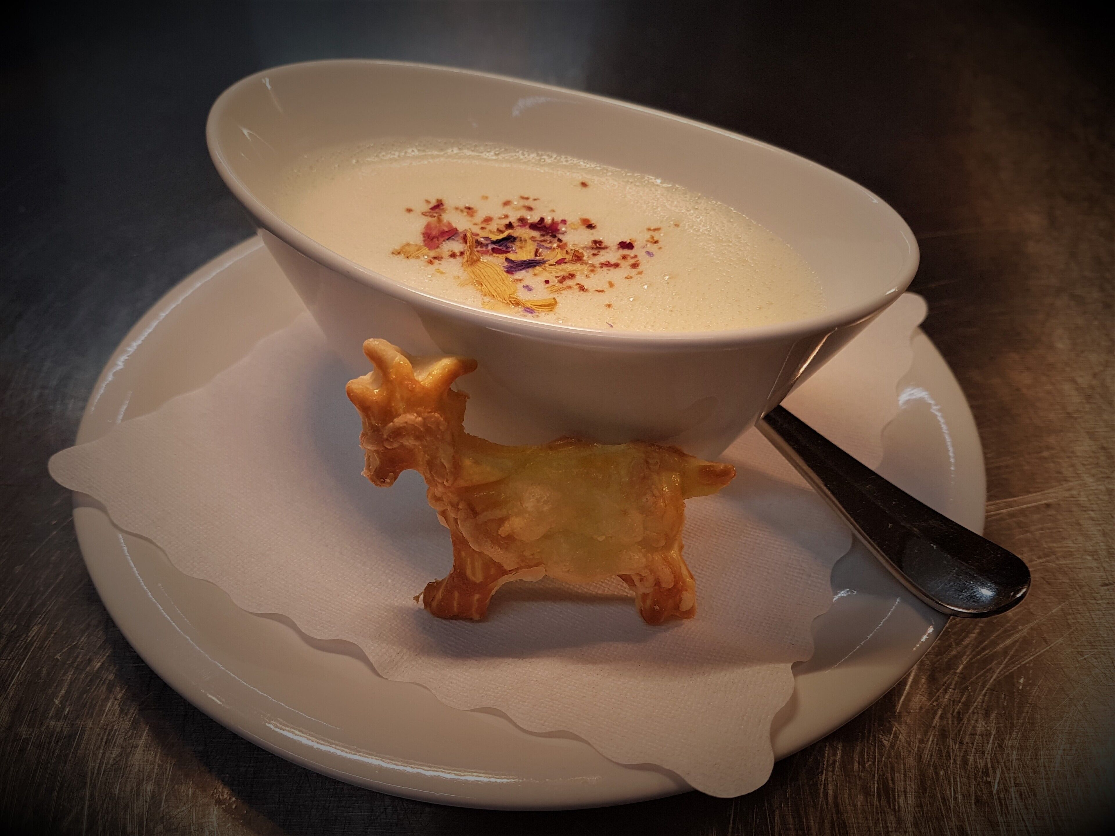 En skål suppe på en hvid tallerken med en ske.
