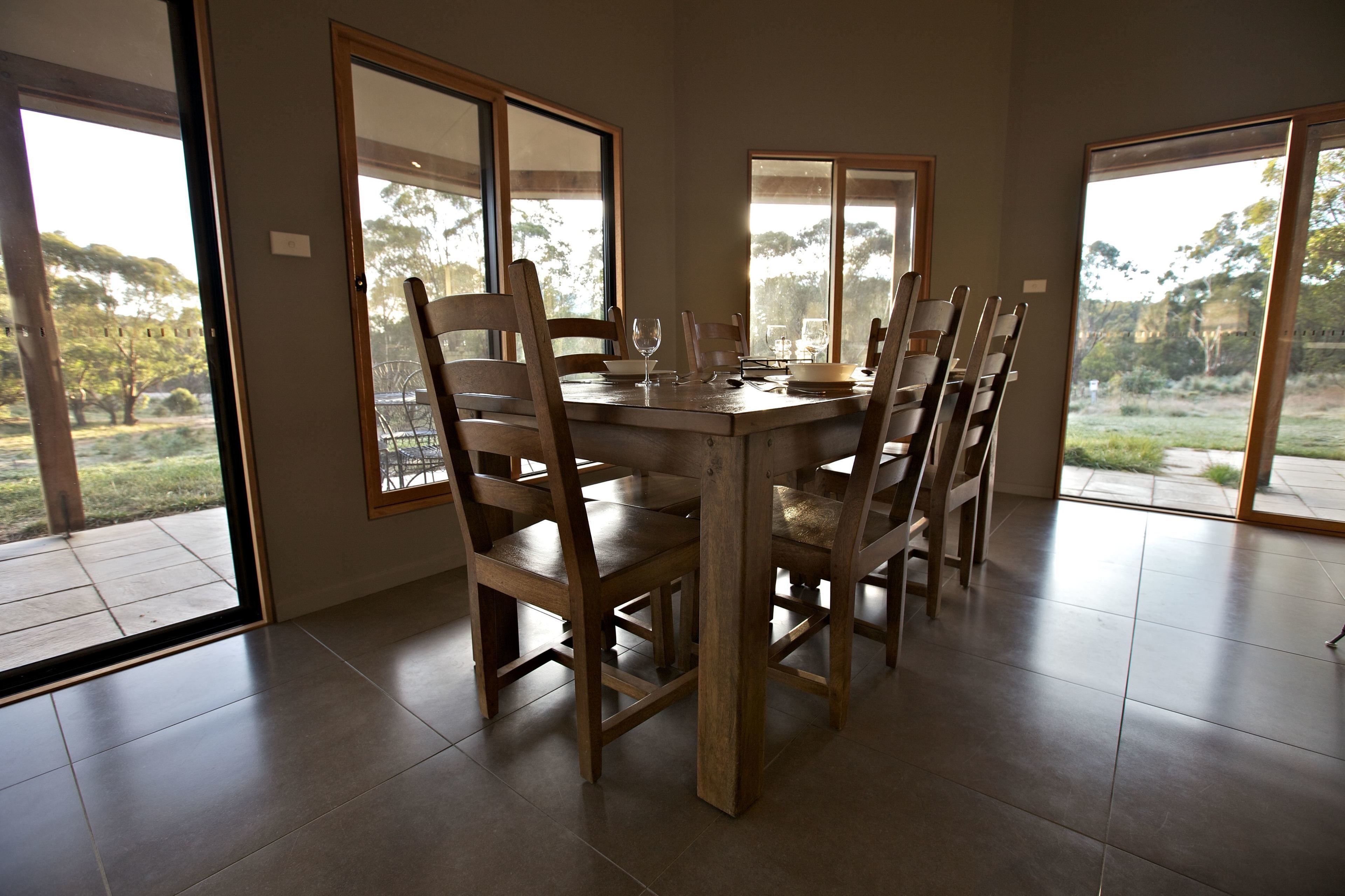 A dining area with a round table, wooden chairs, and large windows offering a view of the outdoors.