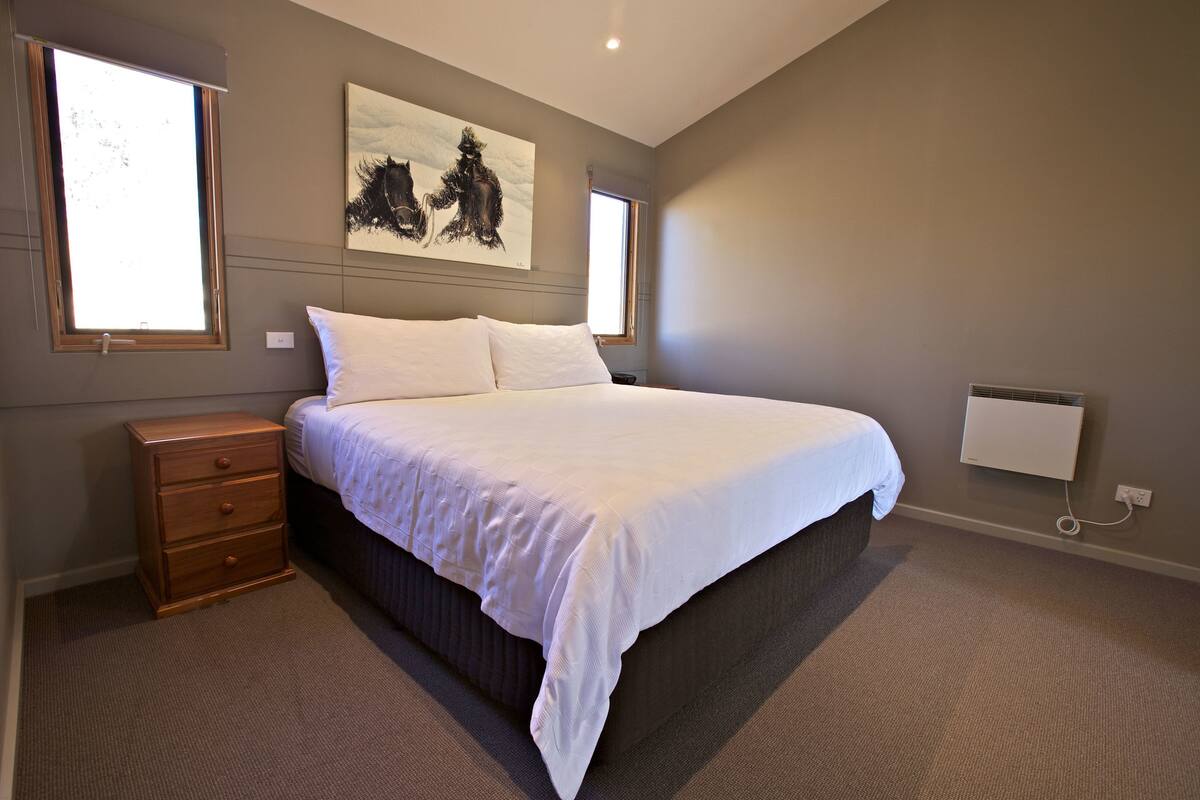 Une chambre avec un grand lit, une table de chevet, un radiateur et un tableau accroché au mur.