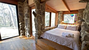A bedroom with stone walls, wooden beams, a large bed with white linens, and a stained glass window. - Snowy Wilderness (Ingebirah)