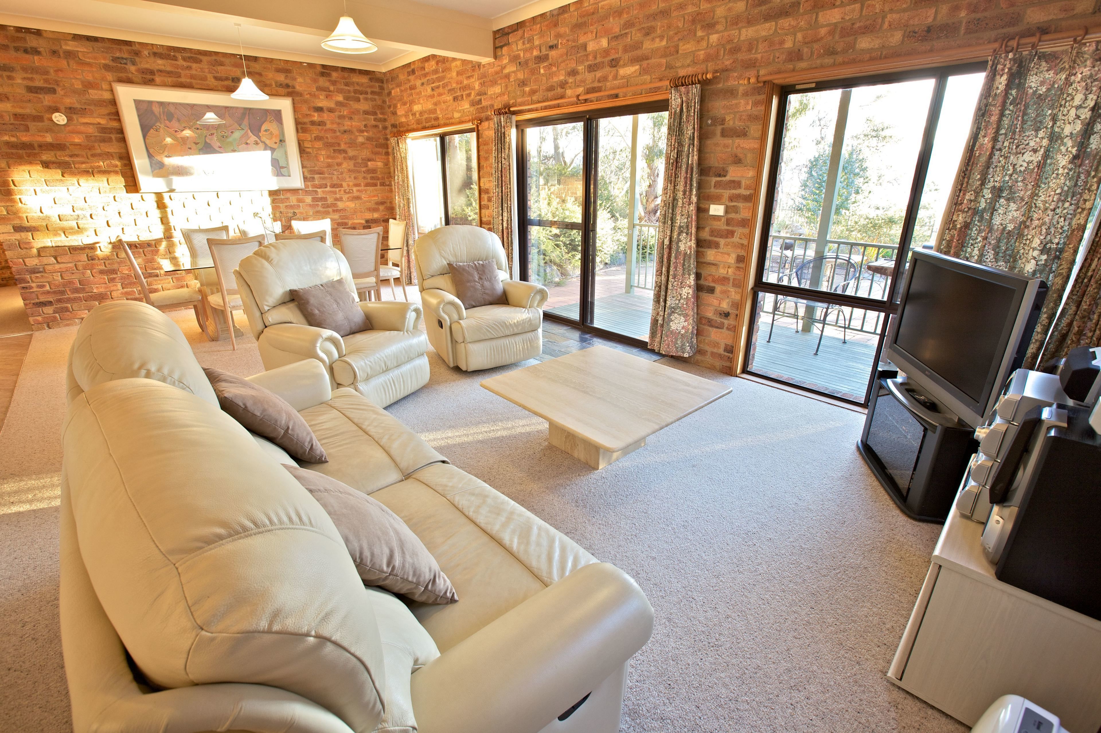A spacious living room with a brick wall, a large sofa set, a coffee table, and a television.