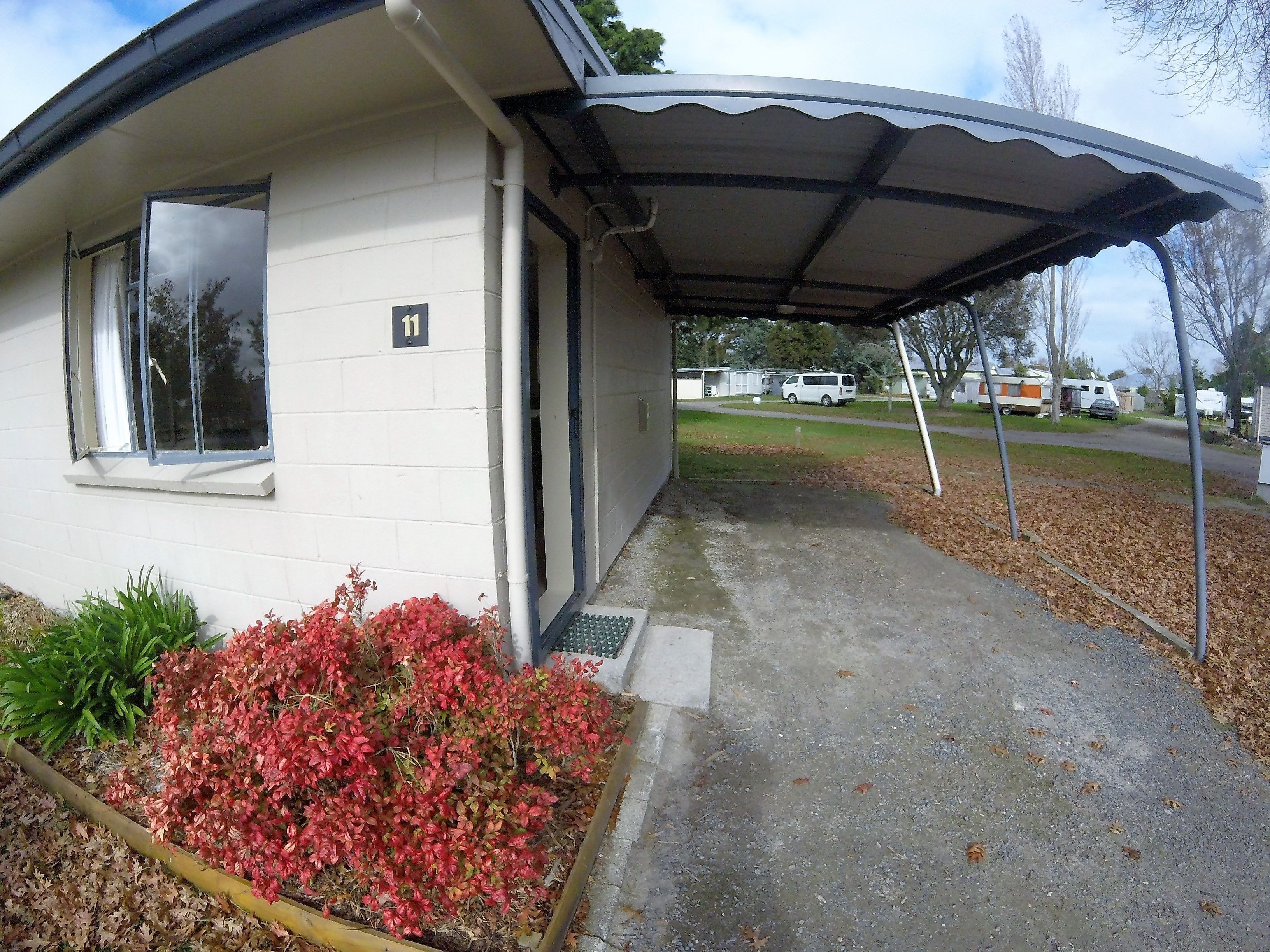 A building with a covered entrance, a number sign, and a driveway leading to a street with parked vehicles.