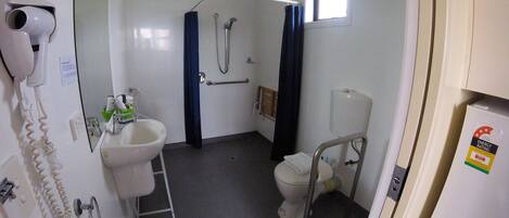 A compact bathroom with a toilet, bidet, and sink. There's a hairdryer on the wall and a window providing natural light.