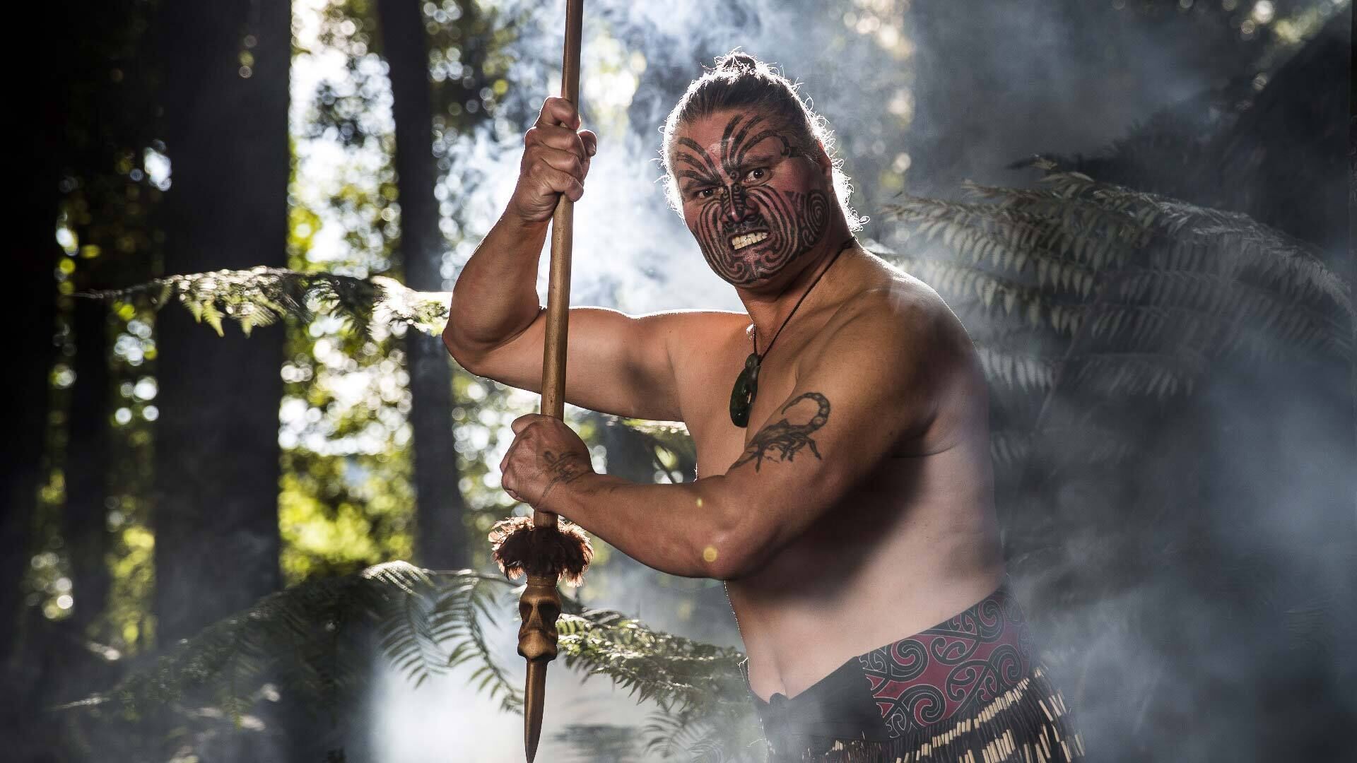 Una persona amb tatuatges tribals agafant una llança a un bosc.