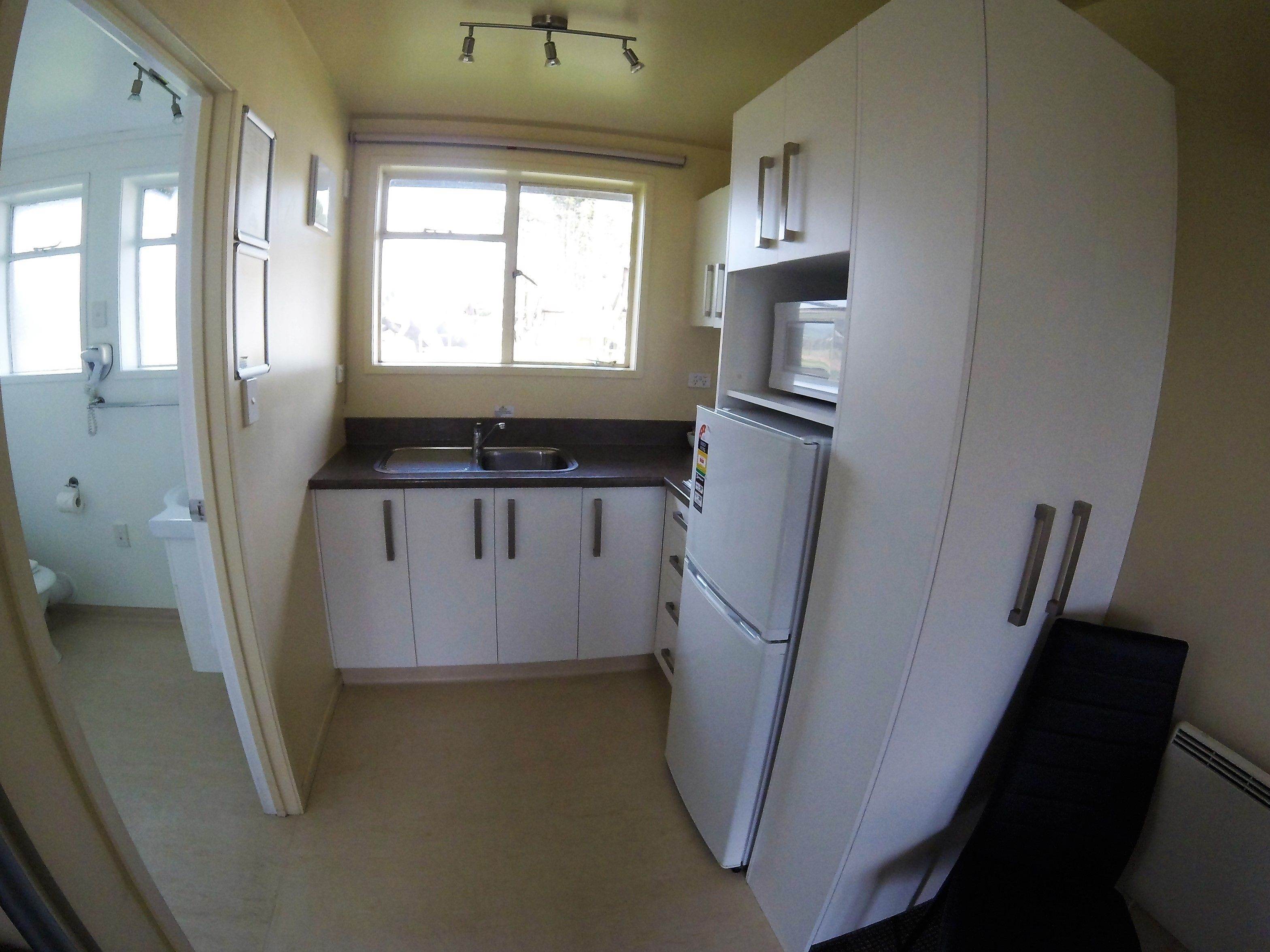 A compact kitchen with white cabinets, a sink, a refrigerator, and a microwave.