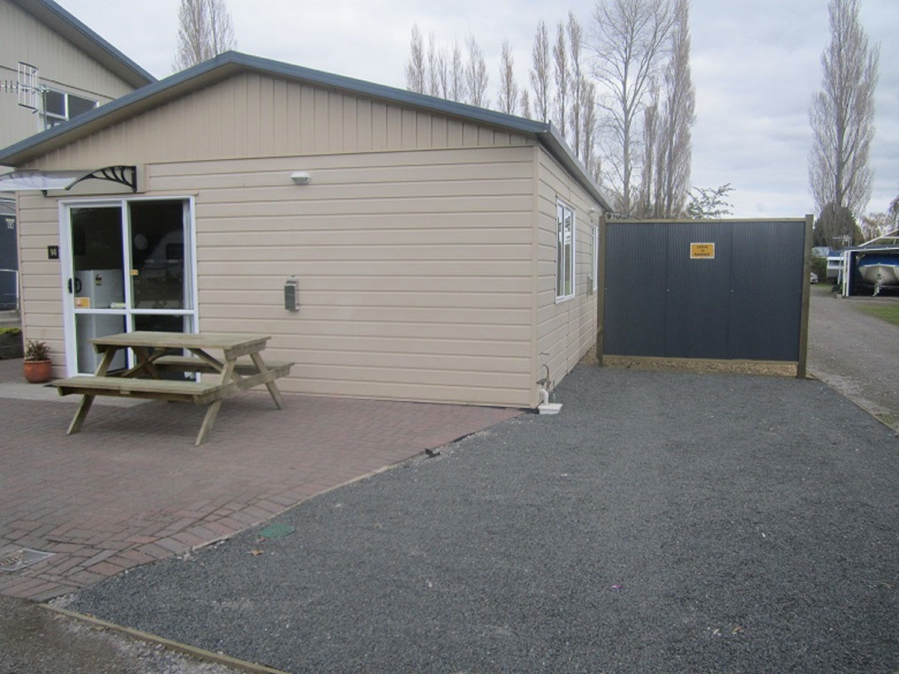 A small, single-story building with a door and windows, a picnic table outside, and a gravel driveway.