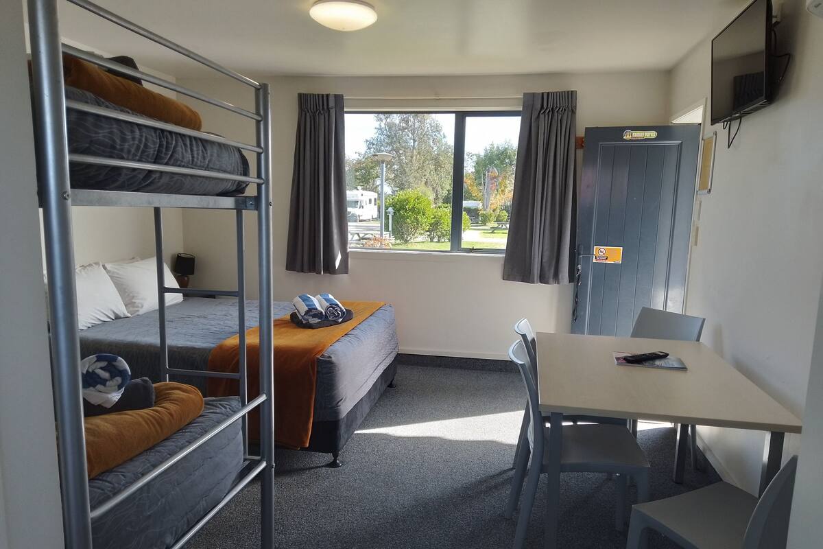 A dorm-style room with bunk beds, a single bed, a desk, and a chair.