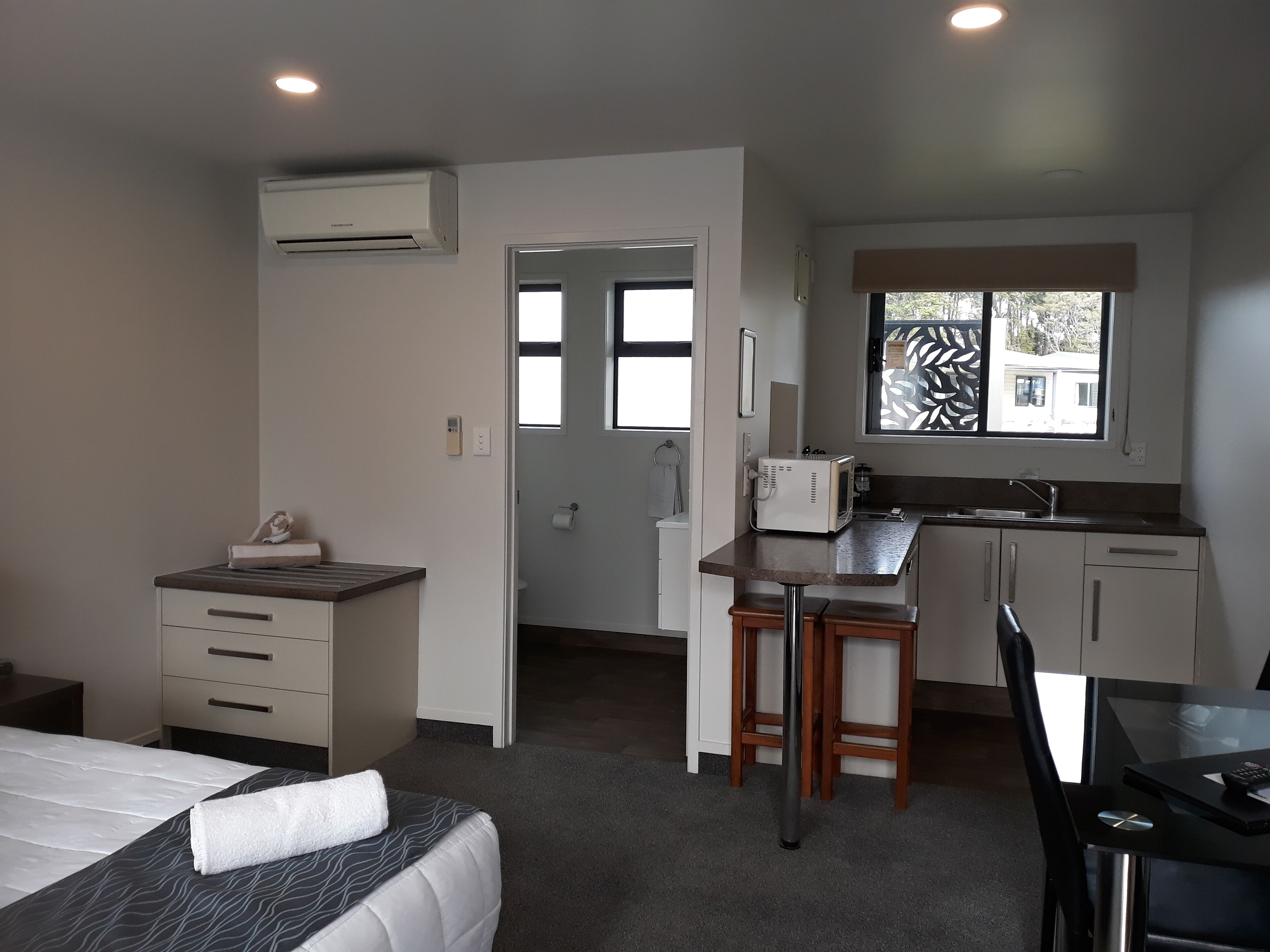 Una habitación de hotel compacta con cama, kitchenette pequeño, zona de comedor y baño.
