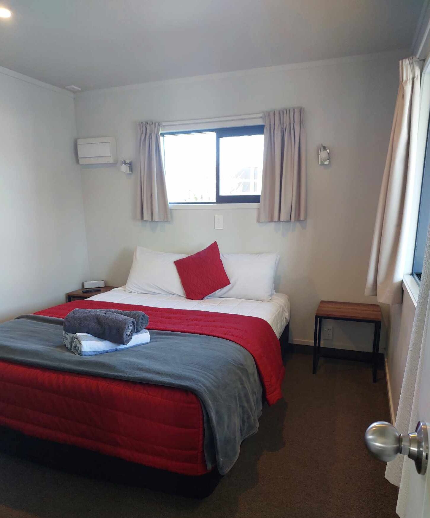 Una camera d'albergo con un letto, un comodino, una finestra con tende e un condizionatore d'aria a parete.