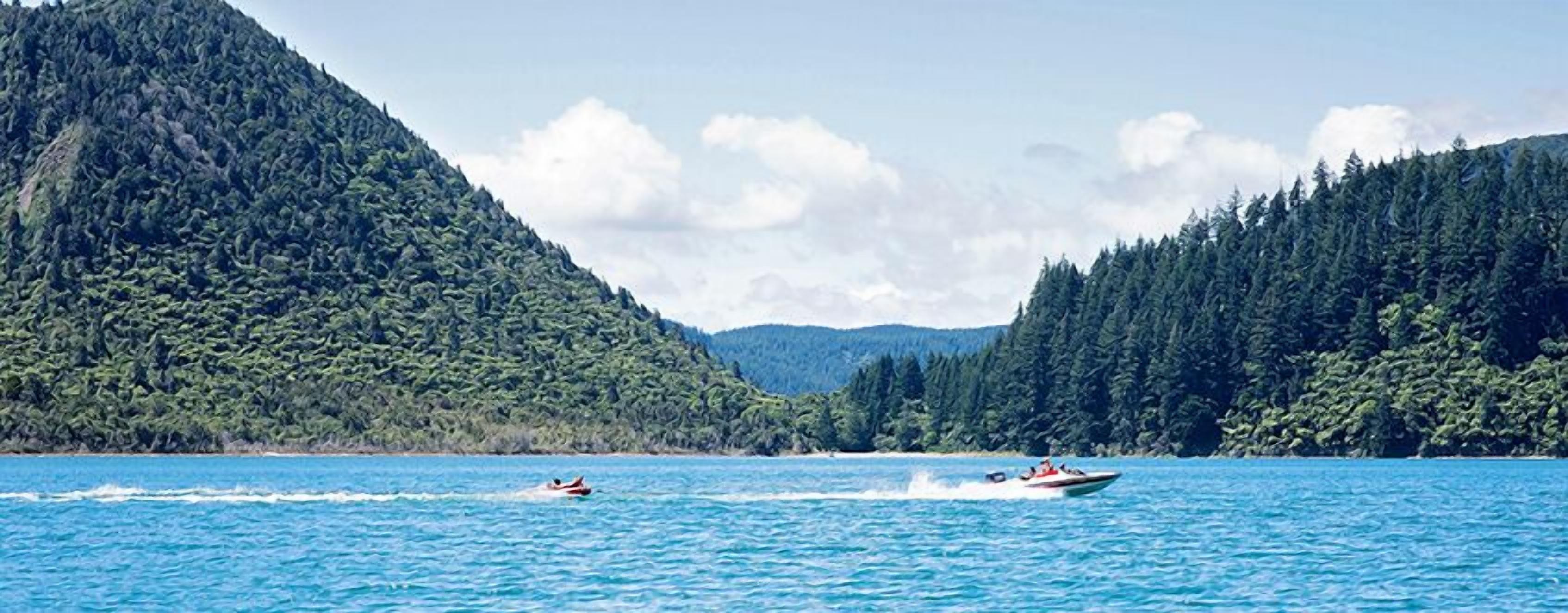 A boat on a calm lake with dense forested hills in the background.