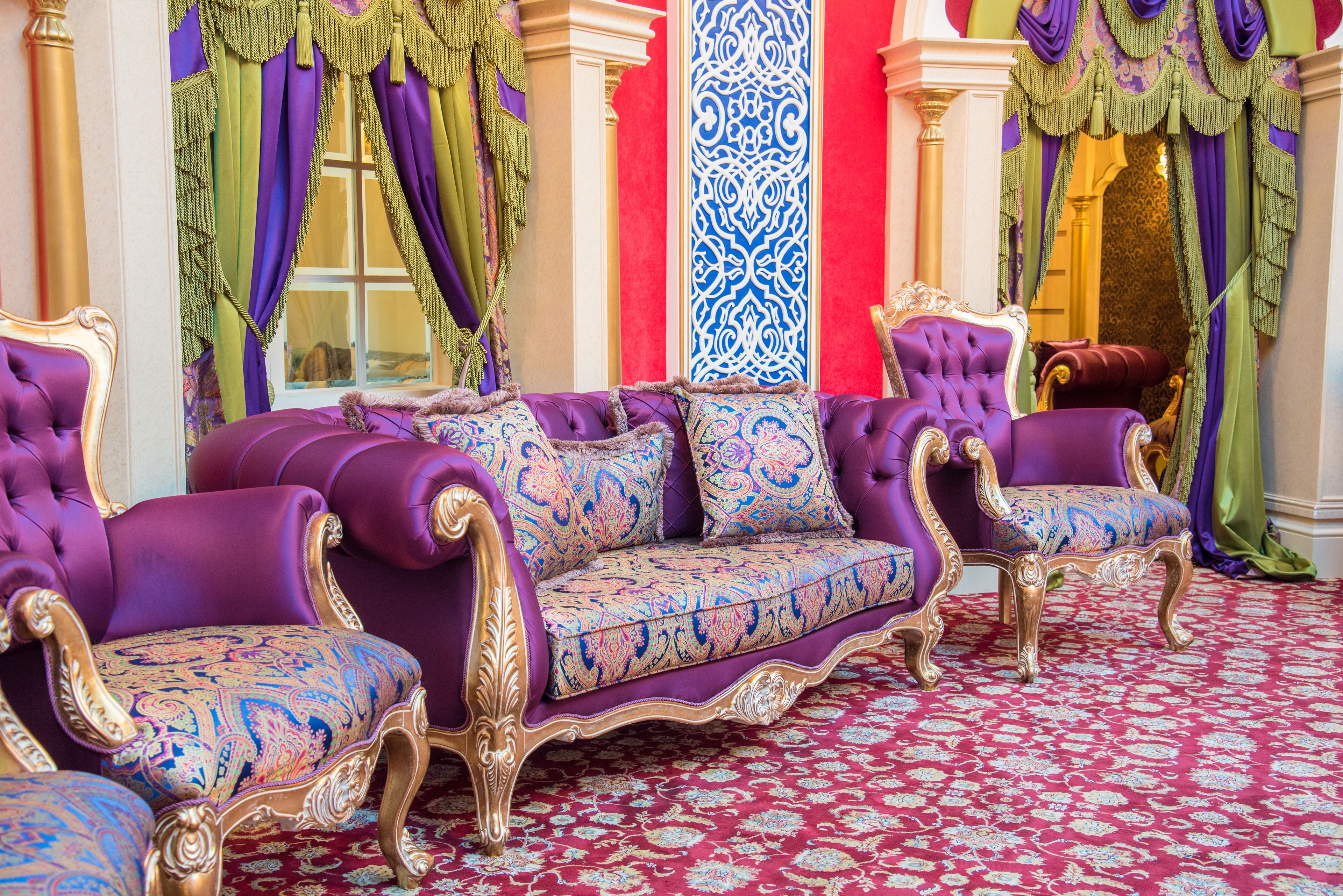 A luxurious room with a purple sofa set, ornate columns, and a patterned carpet.