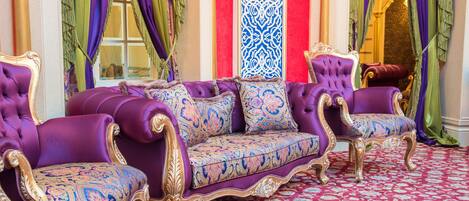 A luxurious room with a purple sofa set, ornate columns, and a patterned carpet.
