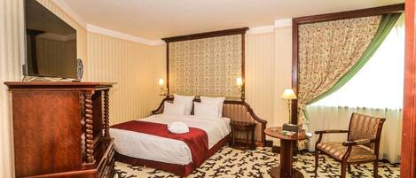Habitación de hotel con una cama grande, un aparador de madera, una mesita con lámpara y una silla.