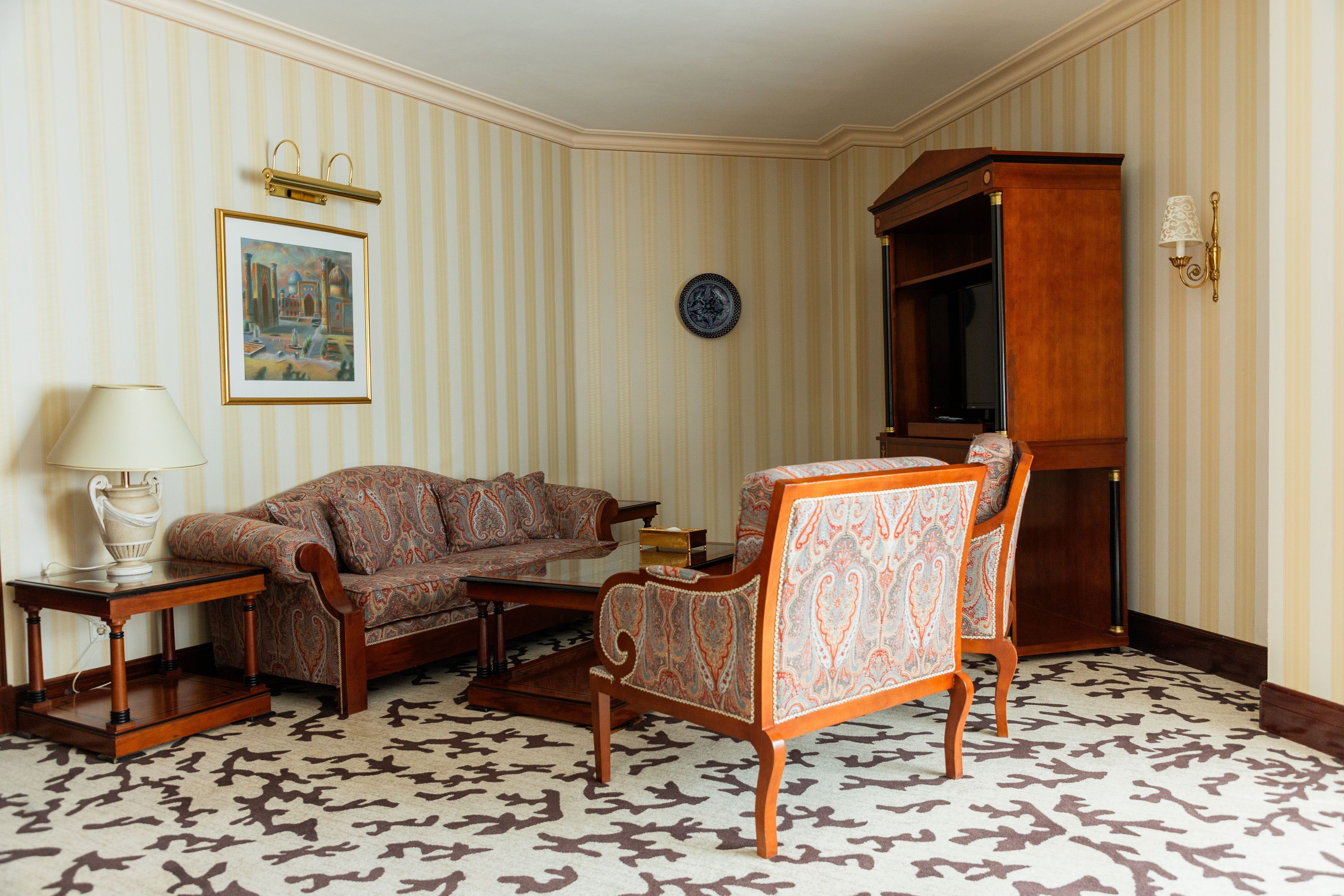 A room with a sofa, armchair, and a wooden cabinet.