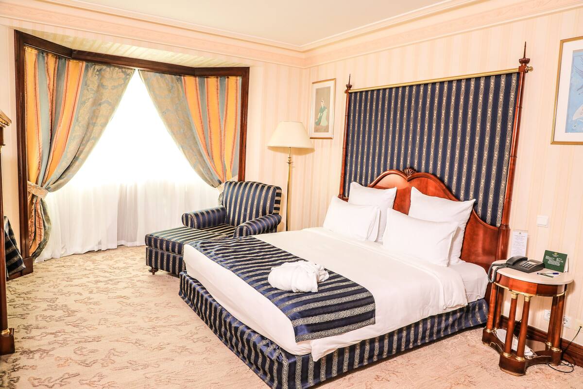 A hotel room with a large bed, a bedside table, a chair, and a window with curtains.