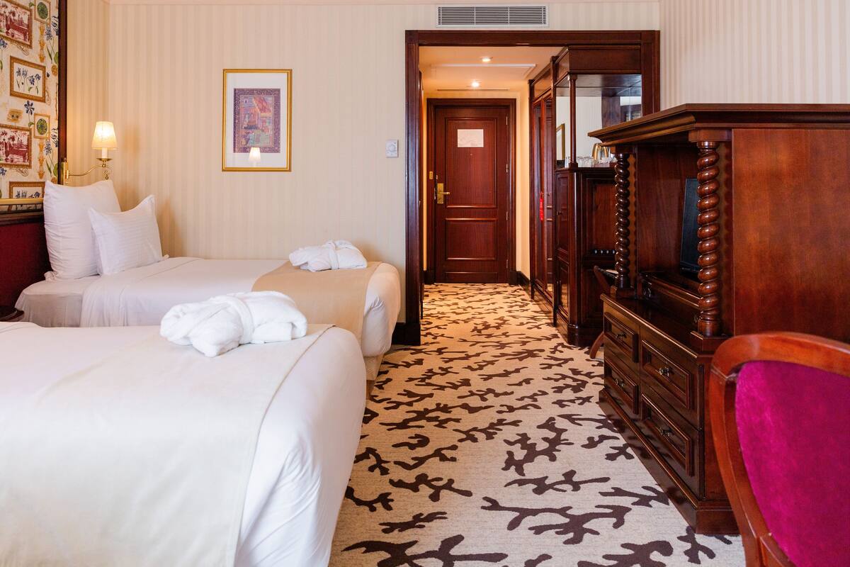 A hotel room with two beds, a wooden dresser, a television, and a patterned carpet.