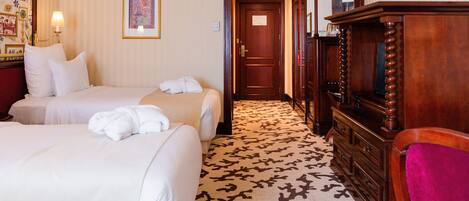 A hotel room with two beds, a wooden dresser, a television, and a patterned carpet.