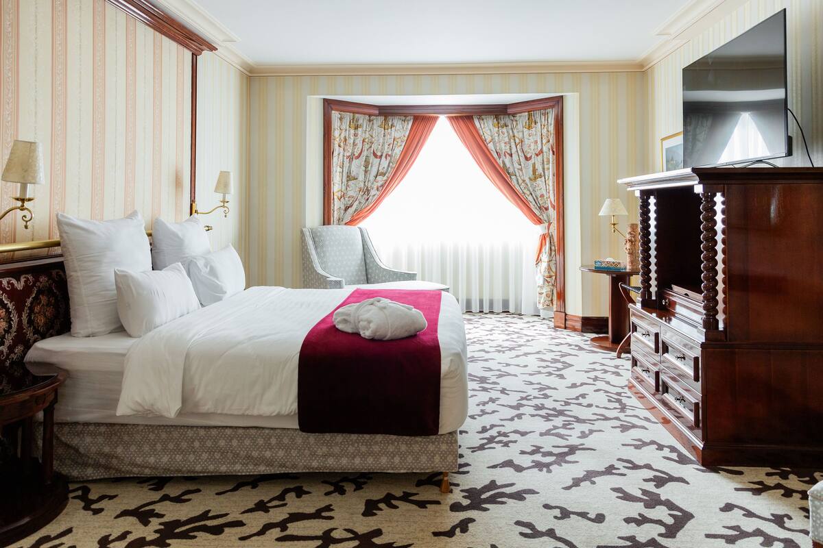 A hotel room with a large bed, a television, a dresser, and a chair.