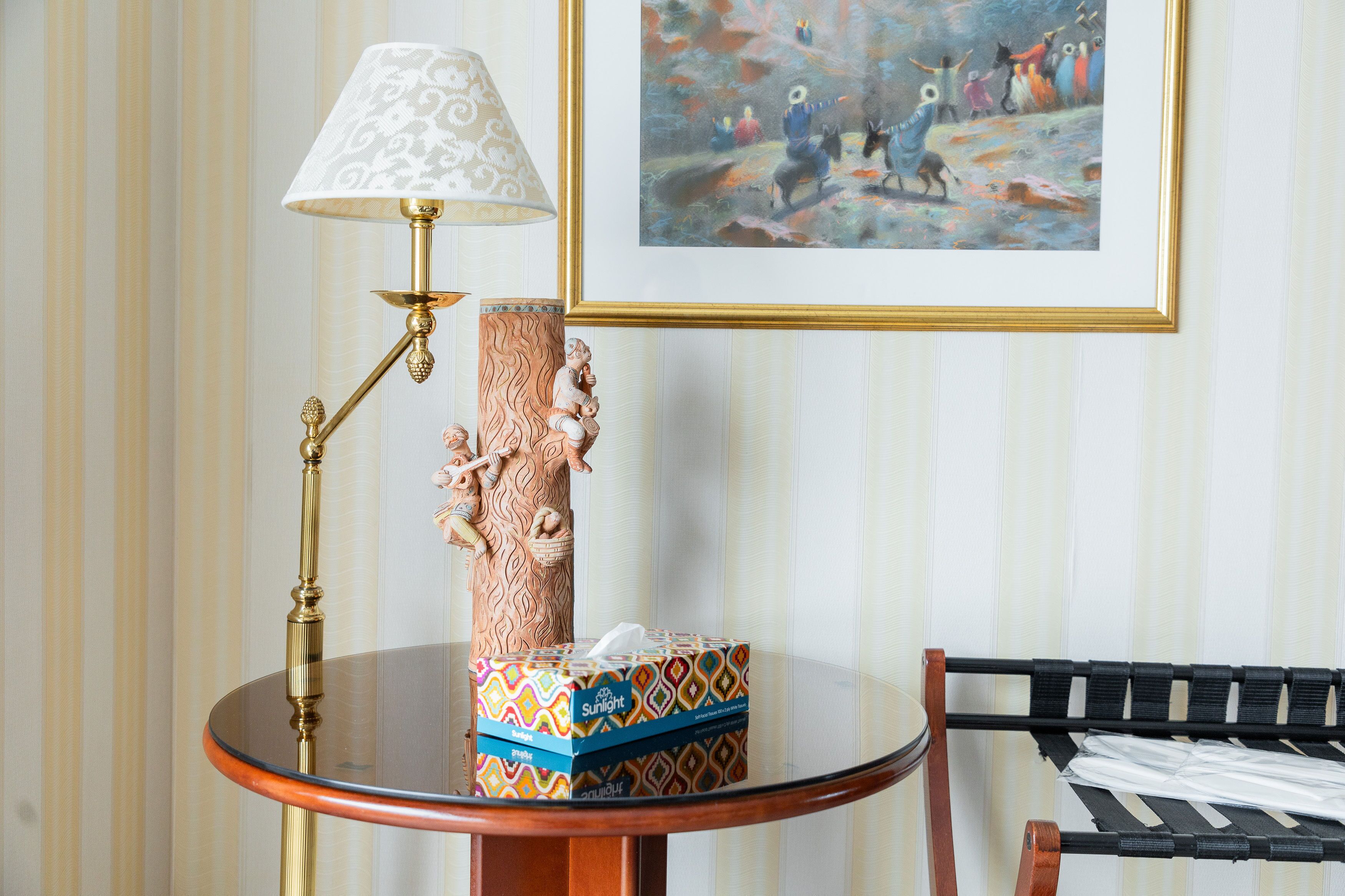 A round wooden table with a brass lamp, a decorative vase, and a patterned box.
