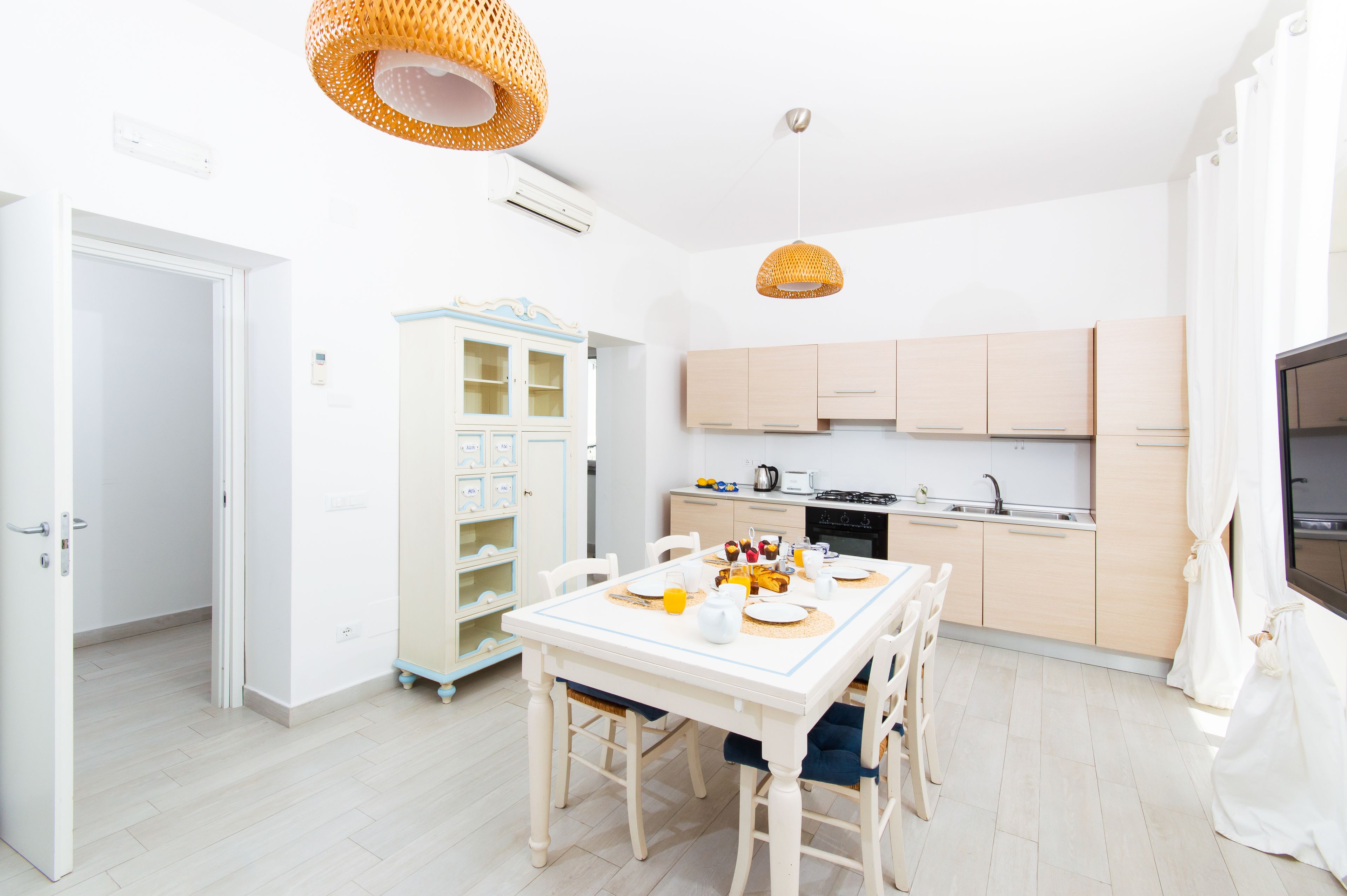 A modern kitchen with light wooden cabinets, a dining table set for four, and a built-in bookshelf.