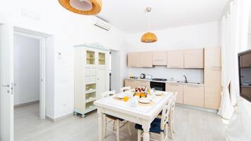 A modern kitchen with light wooden cabinets, a dining table set for four, and a built-in bookshelf.