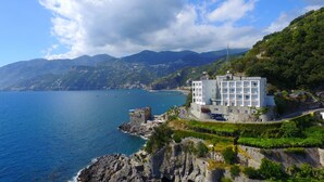 A coastal hotel with a stone tower, surrounded by mountains and the sea.