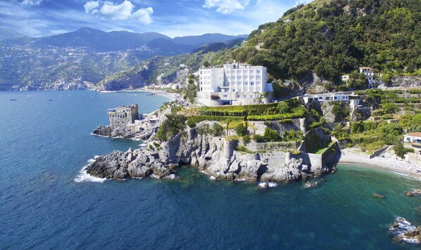 Un hôtel en bord de mer offrant une vue sur l’océan, situé sur une falaise, à proximité d’une structure ressemblant à un château.