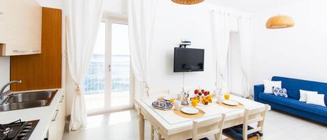 Eine helle Küche mit Essbereich, einem Fernseher und einem blauen Sofa.