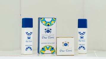 A bathroom with a tiled wall featuring a decorative pattern. There are three products: a body lotion, a shower cap and soap, and a hair wash.