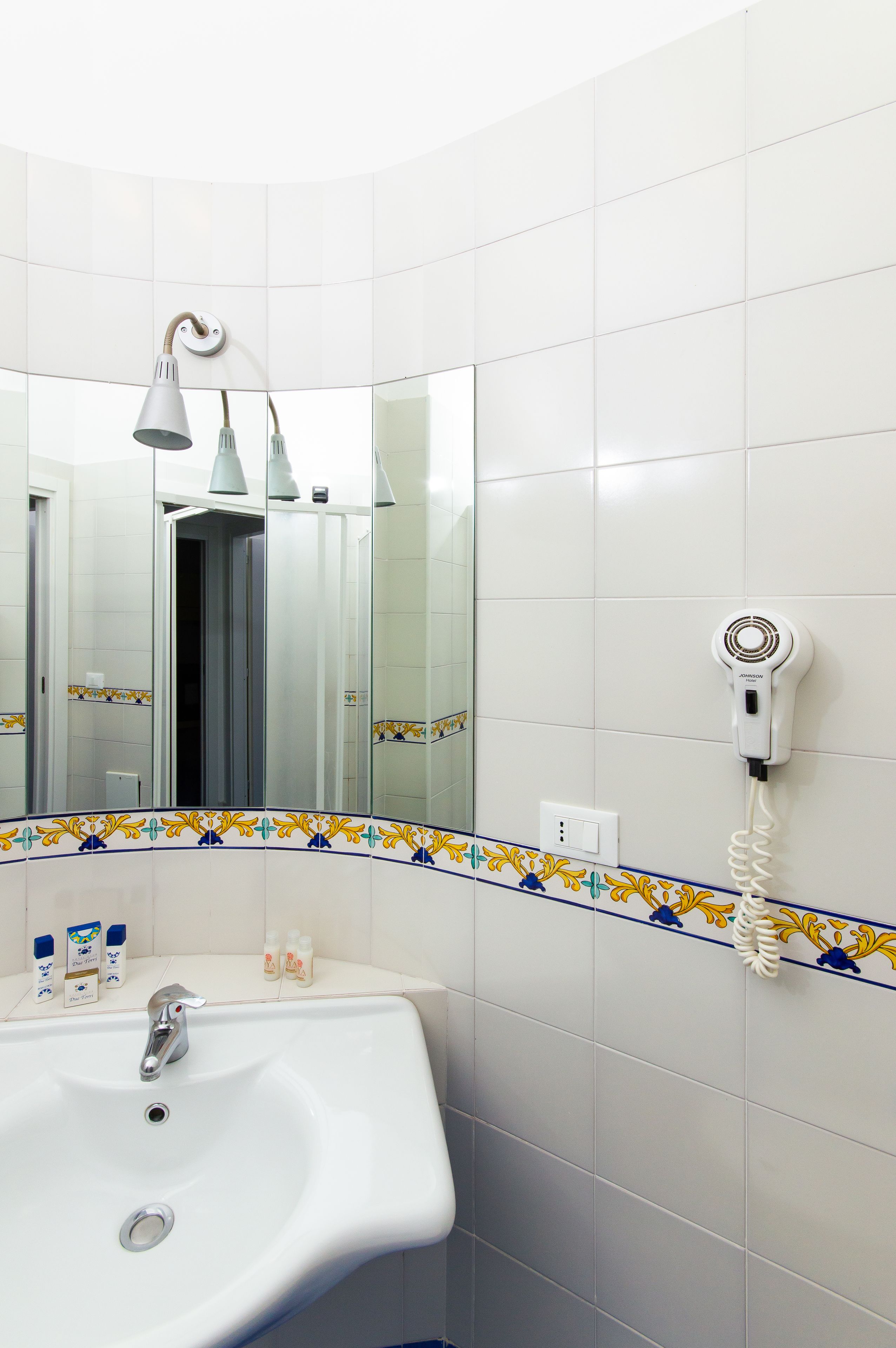 A bathroom with a white sink, a mirror, a hairdryer, and a decorative tile border.