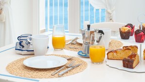 A breakfast table with a white tablecloth, a coffee pot, a glass of orange juice, a plate, and muffins.