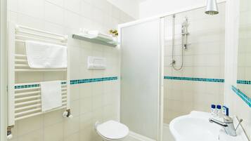 A bathroom with a toilet, sink, and shower. There are towels on a rack and a shelf with toiletries.