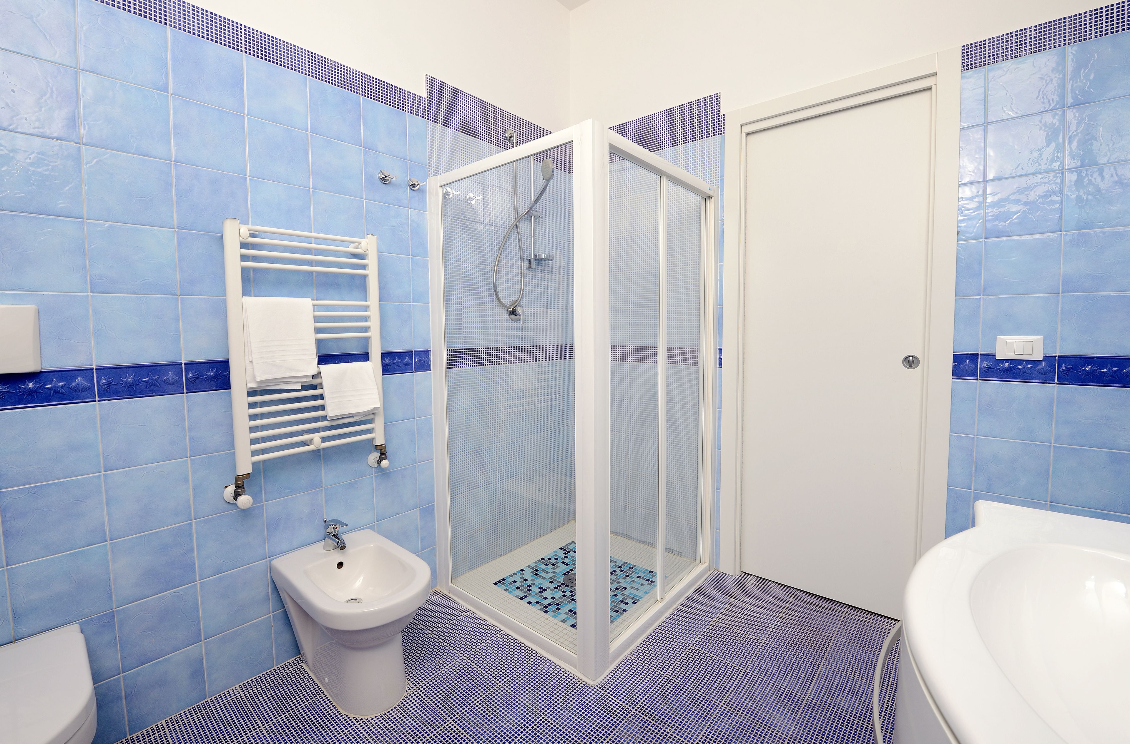 A bathroom with blue tiles, a white sink, a bidet, and a glass-enclosed shower.