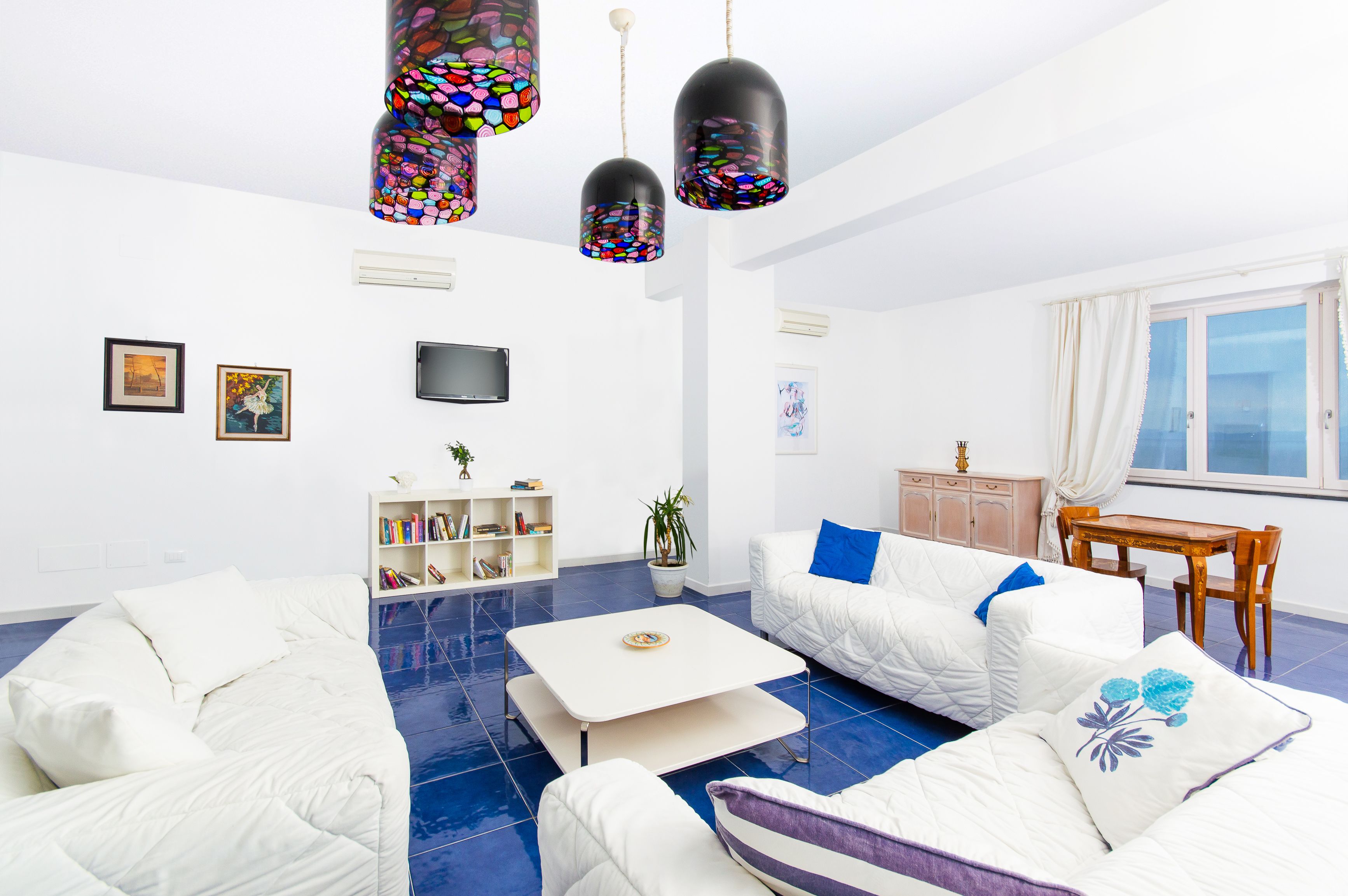 Een moderne woonkamer met witte meubels, een witte salontafel en kleurrijke hanglampen.