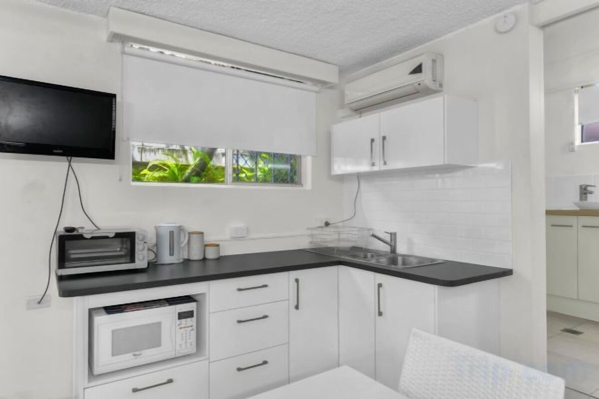 A compact kitchen with white cabinetry, a black countertop, a microwave, a toaster, and a window with a view of greenery.