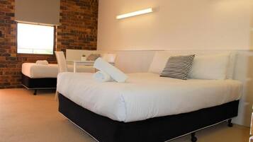 A modern hotel room with a brick accent wall, a large bed with white bedding, a bedside table with a lamp, and a window with a view.