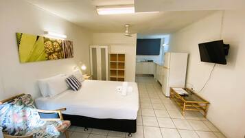 A hotel room with a bed, a desk, a chair, a television, and a kitchenette in the background.