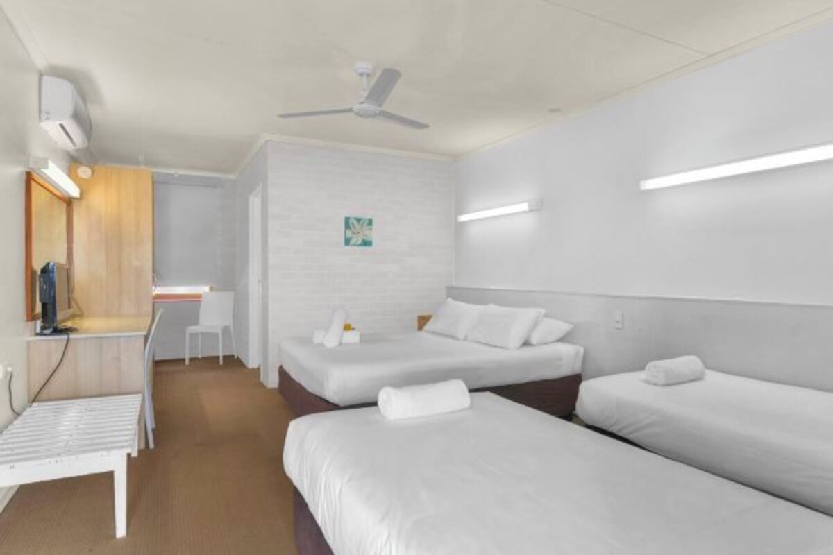 A modern hotel room with two beds, a desk, a chair, and a ceiling fan.