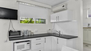 Une cuisine compacte avec des meubles blancs, un plan de travail noir, un four à micro-ondes encastré, un grille-pain et une fenêtre donnant sur un espace verdoyant.