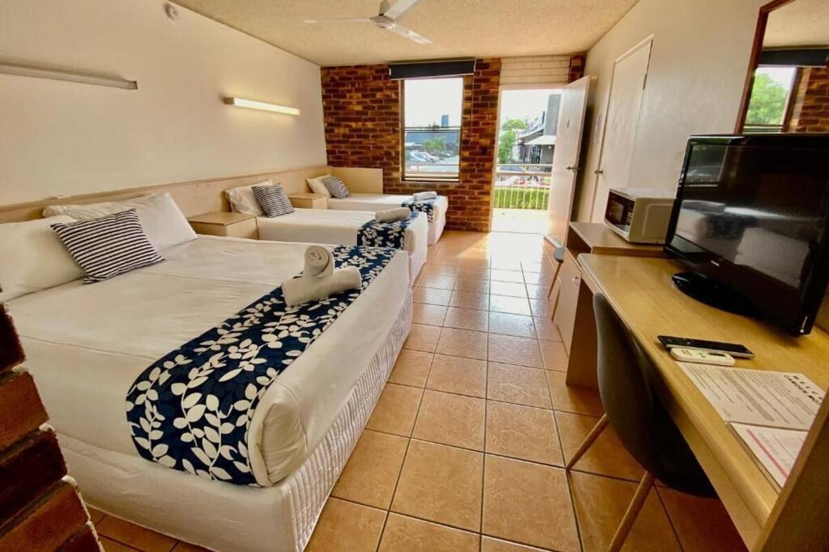 A hotel room with two beds, a desk with a television, and a balcony with a view.